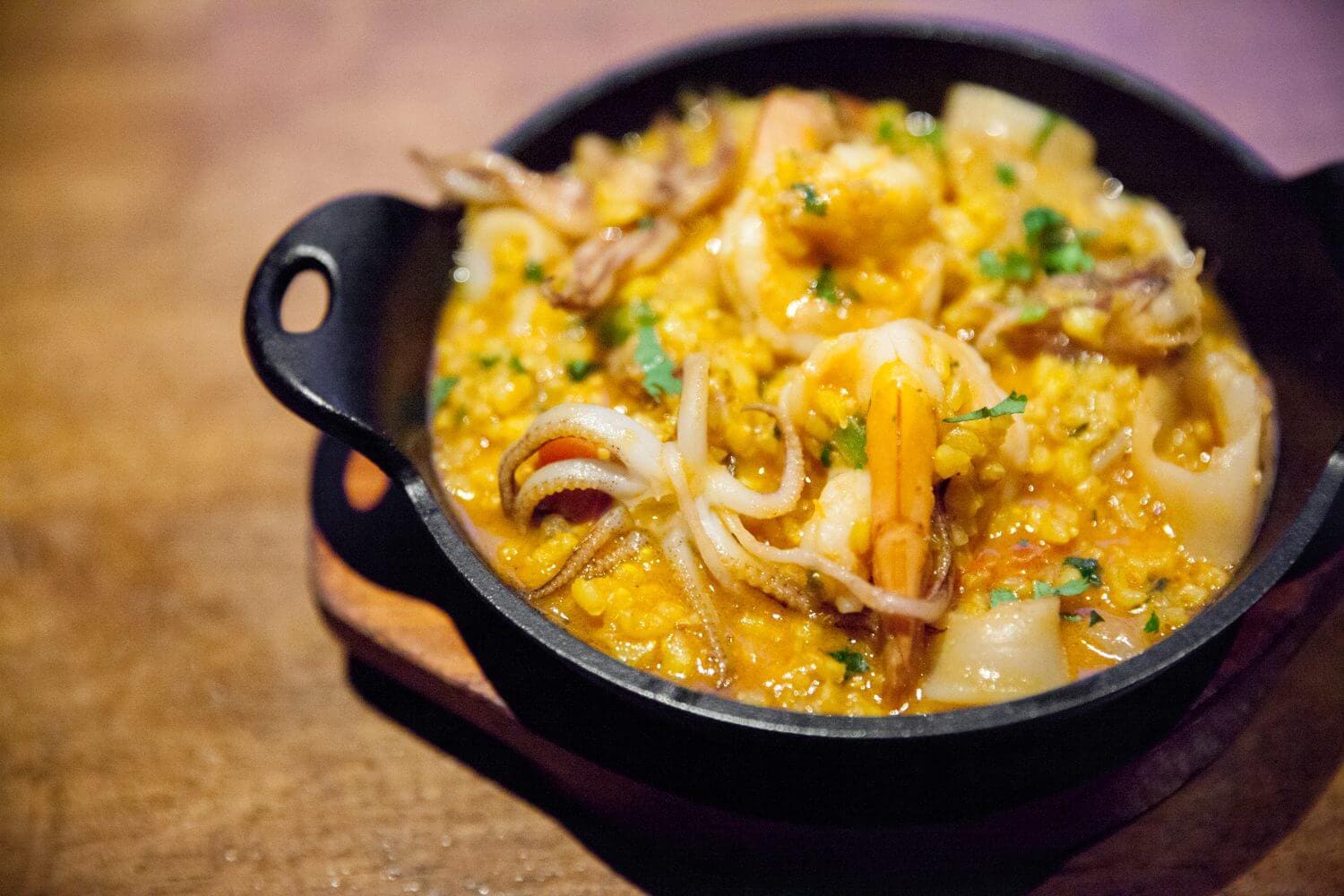 A vibrant seafood paella with shrimp and herbs in a black pan.