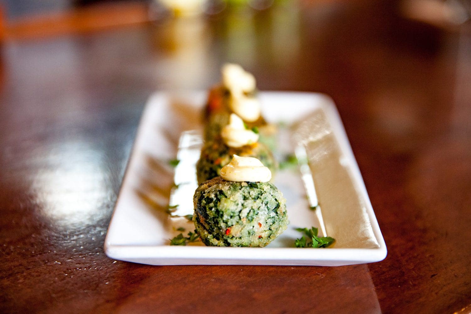 Elegant spinach and cheese balls served on a rectangular white plate.