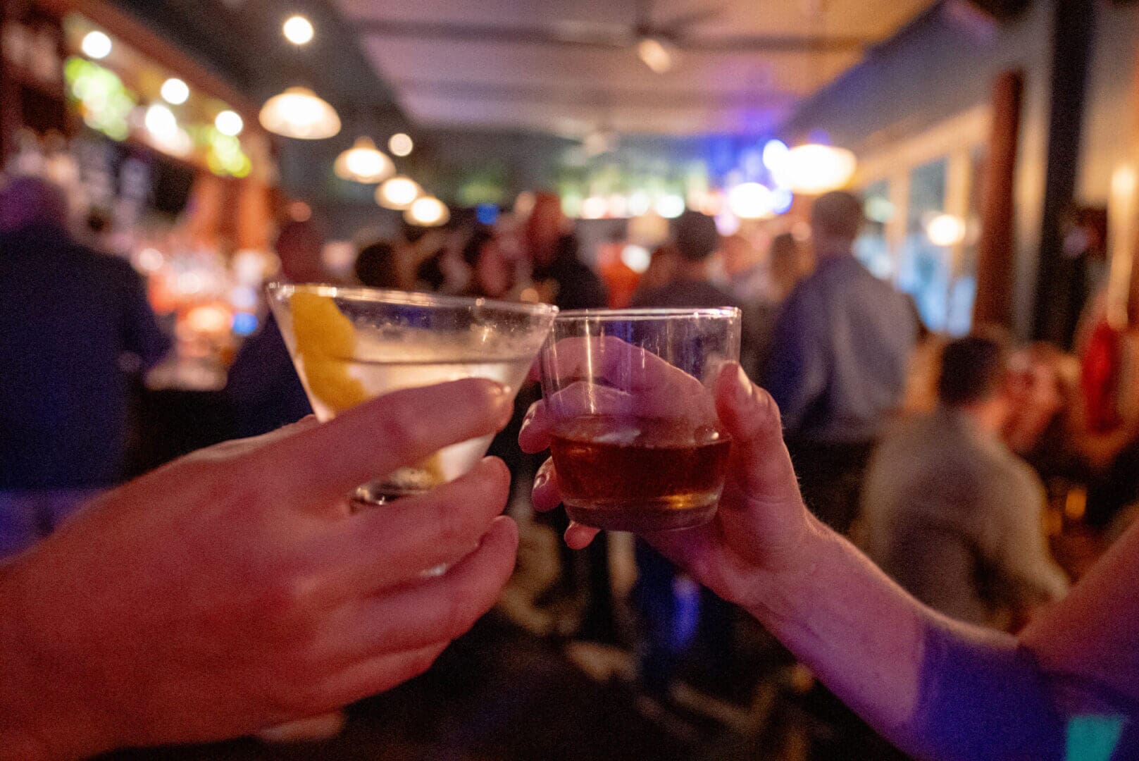 Two people clinking glasses in a lively bar setting.
